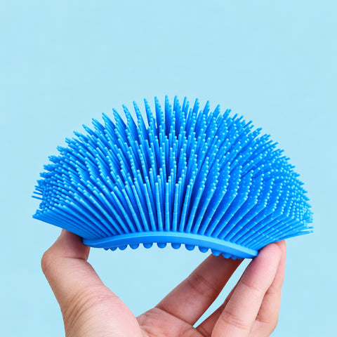 Blue silicone body scrubber held in a curved position showing its long bristles